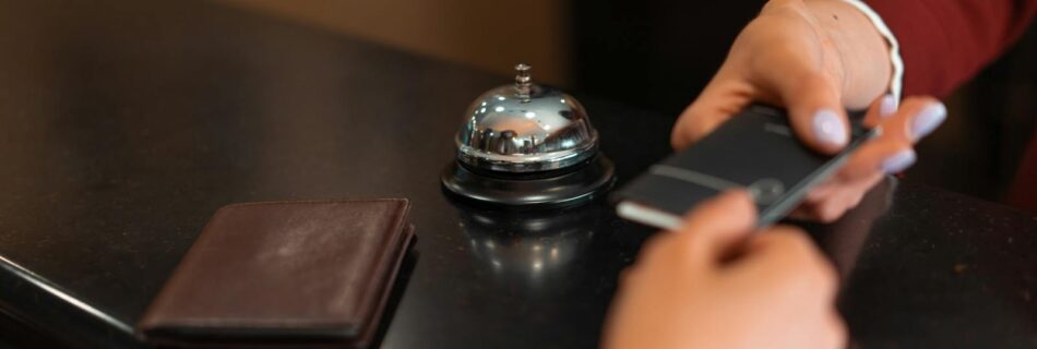 A close-up of a hotel check-in process with a smartphone and card transaction at the reception desk.